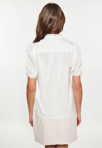 Blusa di raso bianca con maniche a sbuffo corte, colletto arricciato e pieghe posteriori, caratterizzata da una texture liscia e un'orlo curvo.