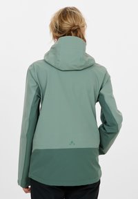 Veste imperméable en deux nuances de vert, dotée d'un col haut, d'une capuche ajustable et d'une texture lisse avec des détails de design minimalistes.