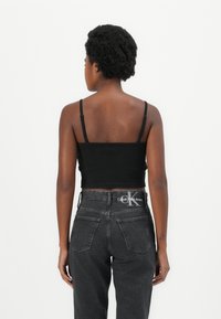 Black ribbed crop top with adjustable straps, paired with high-waisted dark denim jeans. Notable hardware includes the branded waistband.