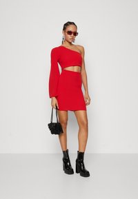 Červený dvojdielny outfit pozostávajúci z crop topu s jedným rukávom a mini sukne s vysokým pásom, doplnený čiernymi platformovými topánkami a malou čiernou kabelkou.