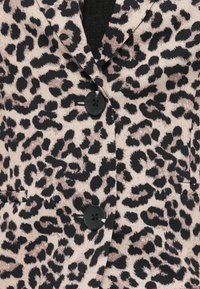 Σακάκι με μοτίβο λεοπάρ, κατασκευασμένο από μαλακό ύφασμα, με μαύρα κουμπιά και εφαρμοστή γραμμή με τσέπες. Φόντο με ανοιχτή υφή.