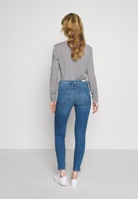 Smala blå jeans med hög midja, med en subtil blekt textur och detaljer på bakfickorna, i kombination med en långärmad topp i svart och vitt mönster.