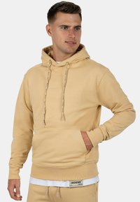 Felpa con cappuccio beige con tasca a marsupio, cordini, polsini a coste e una etichetta sul orlo. Tessuto morbido.
