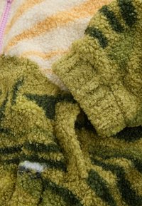 Grønt og beige tekstureret stof med et blødt, løkket strikkemønster med subtile striber og grønne accenter over det hele.