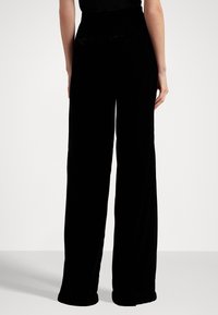 Pantalons larges en velours noir avec taille haute, présentant une texture lisse et deux poches à l'arrière.