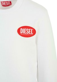 Felpa bianca con una toppa rotonda ricamata rossa che presenta "DIESEL" in testo bianco e "PER UNA VITA DI SUCCESSO" in testo più piccolo sotto.