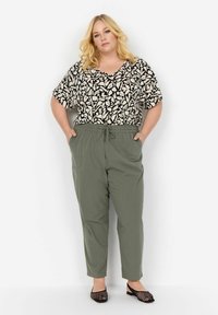 Top patrón en blanco y negro con mangas sueltas, combinado con pantalones de tiro con cordón en verde oliva. Zapatos negros de tacón abierto completan el atuendo.
