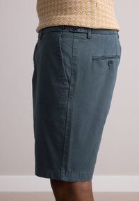 Vyriški tamsiai žalsvi šortai, pagaminti iš medvilnės, su lygiu priekiu, dviem priekinėmis kišenėmis ir viena užpakaline kišene su sagos uždarymu. Lygus paviršius.