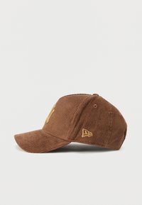 Brown corduroy cap with a curved brim, featuring yellow embroidered logo and accent. Textured surface and structured fit.
