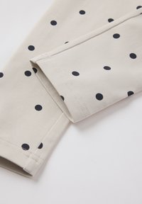 Vaalean beige kangas mustilla pilkuilla, suorat saumat ja sileä pinta. Alareunassa näkyy taitettu reuna.