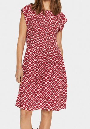 Rotes gemustertes Kleid mit kurzen, flatternden Ärmeln, einem gerafften Oberteil und einem fließenden Rock. Das Muster besteht aus weißen geometrischen Formen.