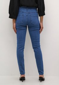 Siniset skinny-farkut korkealla vyötäröllä, takataskuilla ja sileällä denimi-kankaalla, yhdistettynä mustiin korkeakorkoisiin kenkiin.