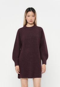 Kötött pulóverruha mély burgundi színben, magas nyakkal, hosszú ballon ujjal és enyhén laza fazonnal, a hemline pedig a comb közepéig ér.