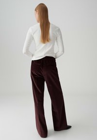 Maglietta bianca a maniche lunghe abbinata a pantaloni in corduroy bordeaux con cintura elastica, tasche laterali e design a gamba dritta.