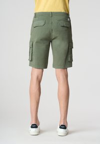 Pantaloni cargo in tessuto verde oliva con vestibilità ampia. Presentano più tasche laterali, tasche posteriori e una sottile trama. Abbinati a sneaker bianche.