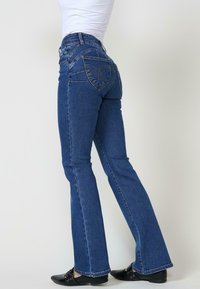 Jeans de mezclilla azul acampanados con una cintura de subida media, que presentan un diseño único en el bolsillo trasero y detalles de costura sutiles.