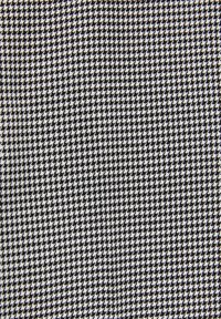 Motif textile noir et blanc avec de petites formes en pied-de-poule répétitives créant un design géométrique texturé.