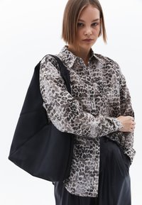 Blůza s leopardím potiskem v béžových a hnědých odstínech, spárovaná s matně černou taškou přes rameno s ostrými designovými detaily.