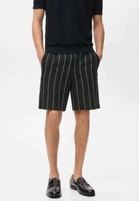 Pantaloni scurți cu dungi negre și linii verticale albe, dintr-un material texturat. Asociați cu un top din tricot negru cu mânecă scurtă și mocasini negri.