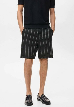 Pantaloni scurți cu dungi negre și linii verticale albe, dintr-un material texturat. Asociați cu un top din tricot negru cu mânecă scurtă și mocasini negri.