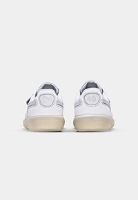 Baskets blanches avec une tige en cuir lisse, des accents en mesh gris et une semelle extérieure semi-transparente. L'arrière présente des chiffres embossés et un détail de logo.