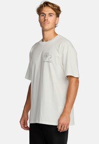 Light beige cotton t-shirt with a round neck, short sleeves, and a black line drawing graphic of a palm tree and text on the front.