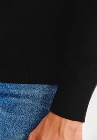 Czarny sweter dziany z prążkowanymi mankietami, zestawiony z niebieskimi dżinsami o lekkiej strukturze, ilustrujący casualowy strój.