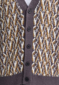 Gros plan d'un cardigan boutonné avec un motif de tricot abstrait marron, blanc et gris et des boutons foncés au centre.