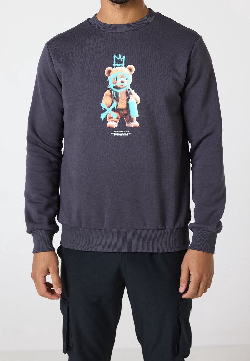 Sweat-shirt gris foncé avec un graphisme d'un ours en peluche tenant une bombe de spray, surmonté d'une couronne et de marques style graffiti bleues.