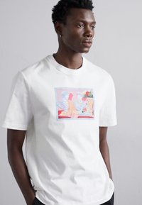 Camiseta de algodón blanca con un estampado gráfico colorido de figuras clásicas con acentos florales. Diseño de manga corta y cuello redondo.