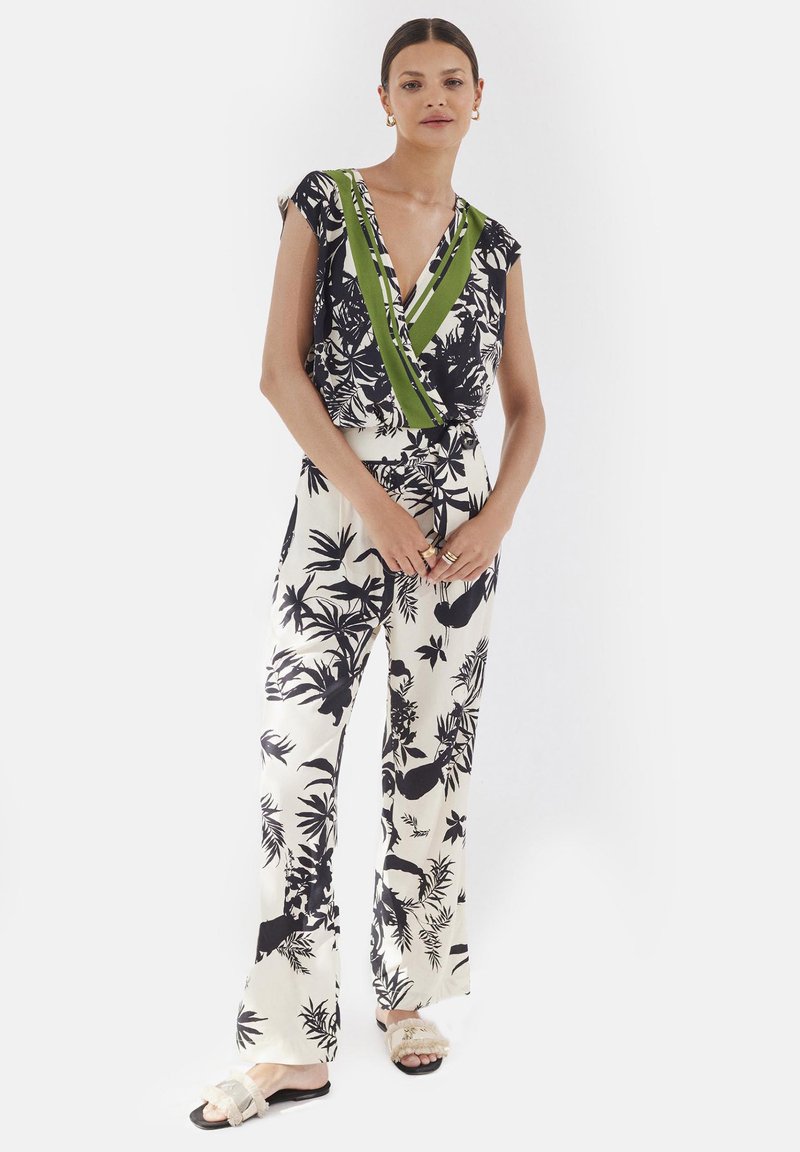 Kombinezon w kwiatowy wzór w czerni i bieli z zielonym i białym dekoltem w kształcie litery V, wykonany z gładkiego materiału; posiada szerokie nogawki i wiązanie w talii.