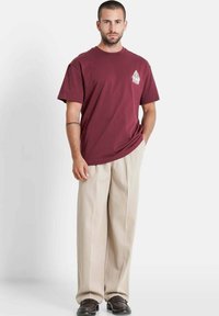 Maroon cotton t-shirt with a round neckline and short sleeves, paired with beige wide-leg pants and black shoes. Simple design and solid colors.