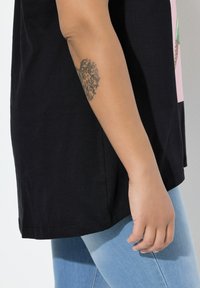 Czarny bawełniany t-shirt z krótkimi rękawami, o luźnym kroju i z nadrukiem graficznym. Połączony z jasnoniebieskimi dżinsami, ukazującymi gładką teksturę denimu.