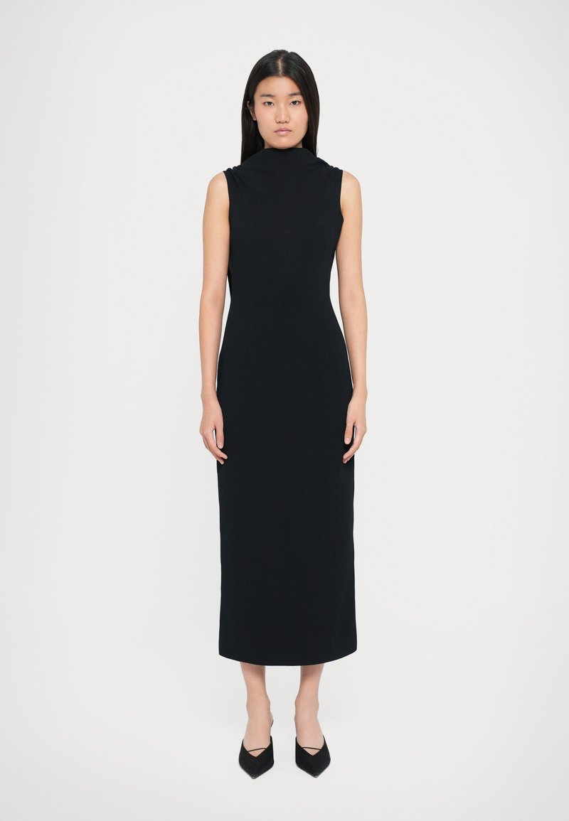 Vestido midi preto sem mangas com gola alta, silhueta ajustada e textura suave. Usado com sapatos de salto fino pretos.