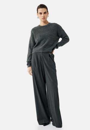 Grauer Strickpullover mit gerippter Textur, kombiniert mit hochtaillierten, weiten, schiefergrauen Hosen mit Gürtelschlaufen-Details.