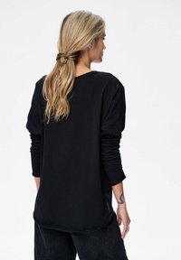 Zwarte lange mouwen shirt met een relaxte pasvorm, voorzien van een afgeronde zoom en omgeslagen mouwen. Gladde textuur, minimalistisch ontwerp.