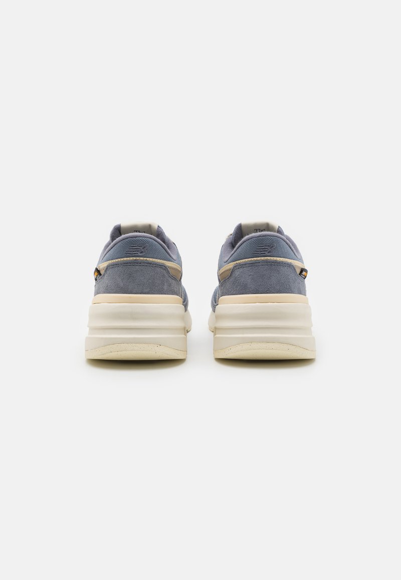 Blaue Wildledersneaker mit einer dicken weißen Sohle, ausgestattet mit einer cremefarbenen Akzentfarbe und dezentem Branding an der Ferse und der Seite.