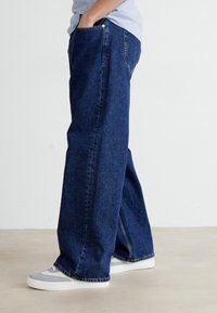 Volné tmavě modré denimové džíny širokého střihu s uvolněným fit, s klasickým pětipocket designem a jemnými švy.