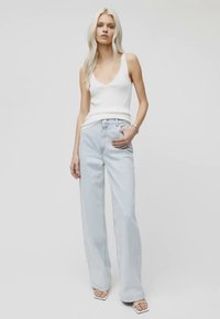 Valge ribaga kampsun on kombineeritud helesiniste laia säärega teksadega. Riietus sisaldab minimaalset metalli ja pehmeid tekstiile. Valged avatud nina kingad.