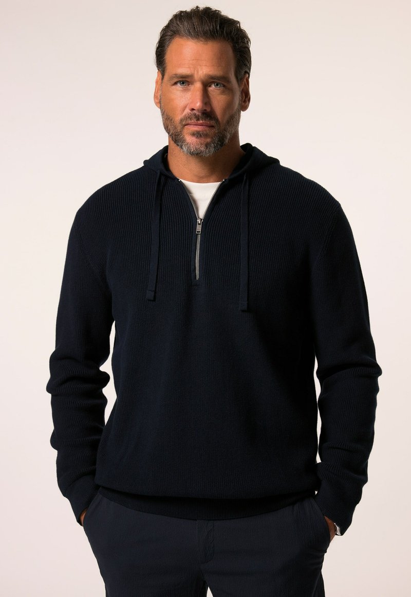 Donkerblauwe hoodie met rits, voorzien van ribbeltextuur, lange mouwen en een capuchon met trekkoord. Gelaagd over een wit shirt.