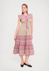 Maxikjole i lys grønn stoff med rosa blomsterprint, volanger på ermene, snøring i livet og et lagdelt nederdel.