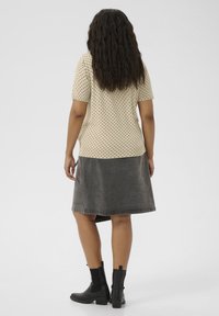 Haut beige à pois avec des manches courtes, associé à une jupe en denim grise. Le modèle porte des bottines noires, avec un design texturé.