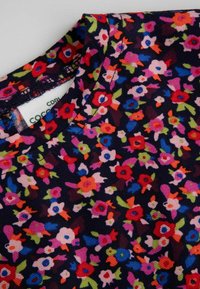 Tkanina w kwiatowy wzór na ciemnym tle, z różowymi, czerwonymi i niebieskimi kwiatami. Okrągły dekolt z widocznymi detalami szycia.