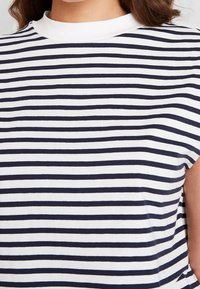 T-shirt in cotone a righe con linee orizzontali bianche e blu scuro, caratterizzato da un collo rotondo e maniche corte, con una texture di tessuto liscia.