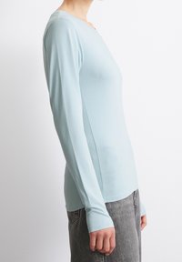 Vaaleansininen pitkähihaisen puuvillapaita, jossa on pyöreä pääntie ja vartalonmyötäinen leikkaus, pehmeä tekstuuri ja saumattomat kalvosimet. Yhdistetty harmaisiin housuihin.