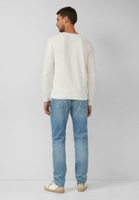 Witte gebreide trui met lange mouwen, gecombineerd met lichtblauwe jeans. De trui heeft een ronde halslijn en een aangesloten ontwerp.