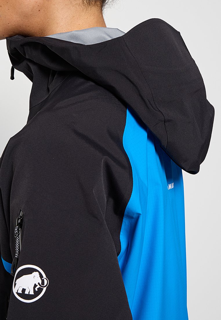 Wasserabweisende Jacke mit schwarzem Körper und blauen Akzenten, ausgestattet mit einer Reißverschlusstasche und einem Logo-Patch auf dem Ärmel. Kapuzen-Design.