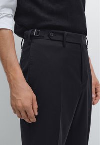 Black pants with a smooth texture, featuring a belt with a silver buckle and button detail. No visible patterns, tailored fit.