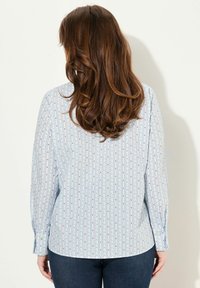 Camisa de botones azul claro con rayas verticales y pequeños patrones florales. Mangas largas y corte relajado; hecha de tela suave.
