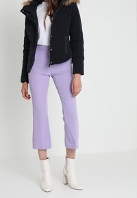 Černá prošívaná bunda s kapucí lemovanou kožešinou, bílý top, lila krátké kalhoty a bílé kotníkové kozačky na podpatku.